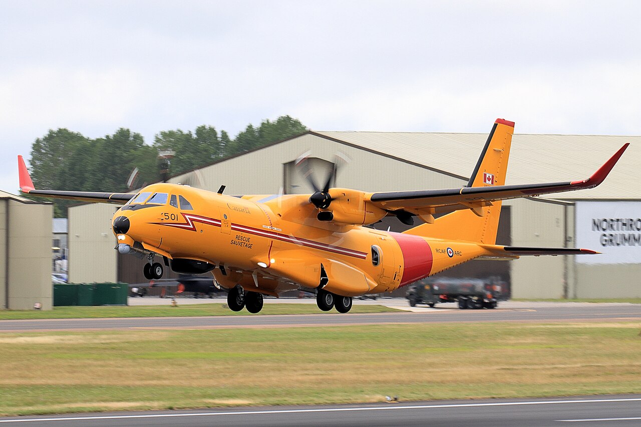 A yellow and red Canadian CC-295 Kingfisher lifting off, with landing gear extended.