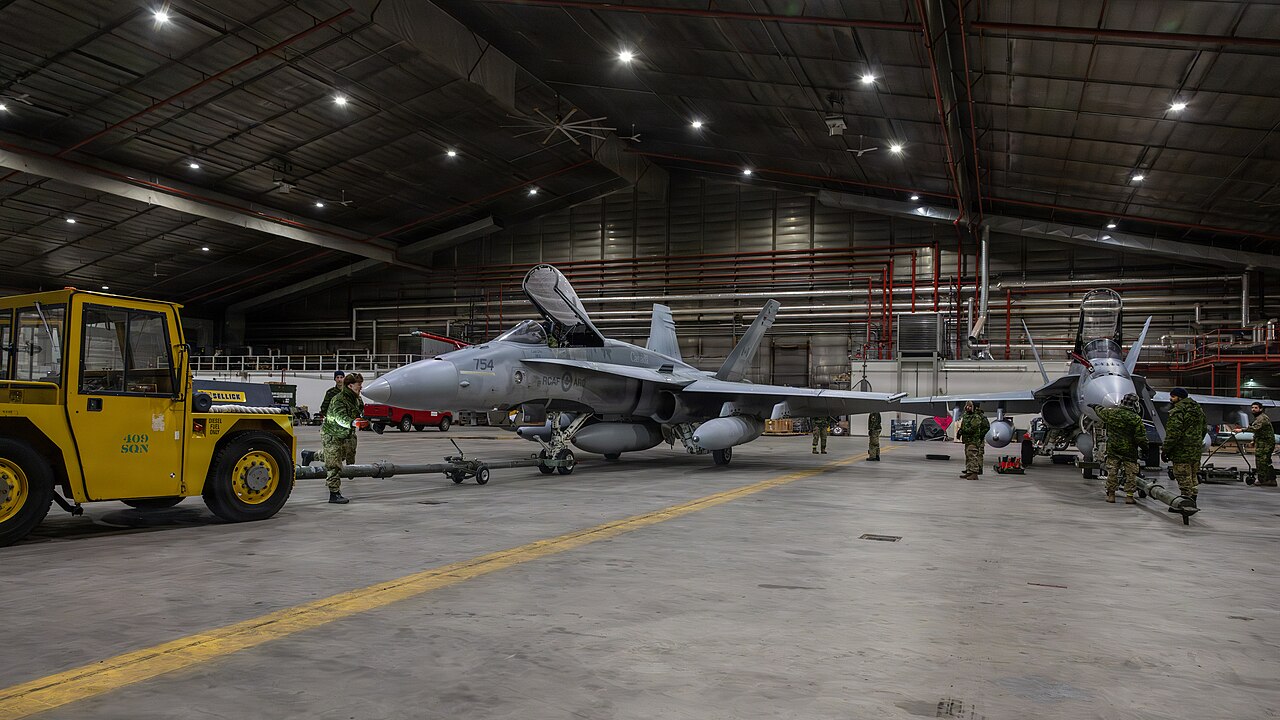 Two Canadian CF-188 Hornets in a hangar with personnel and ground-support equipment.