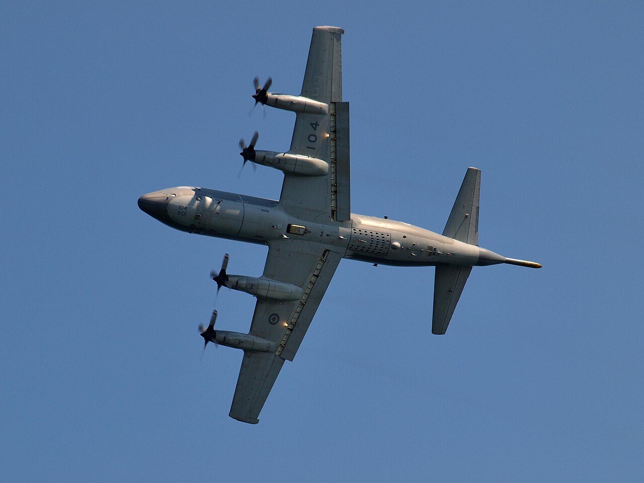 A Canadian CP-140 Aurora banking in flight, showing its four propellers and underside.